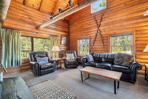A log cabin interior with a leather sofa, armchairs, a coffee table, and a patterned rug.