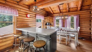 A log cabin interior with a kitchen area, wooden walls, and a dining table with chairs. - Hilltop Log Cabin Retreat with Hot Tub & Direct Trail Access Near Lead (Lead)
