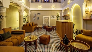 Un'hall d'albergo con pavimento a scacchi, divani, zona bar e un balcone.