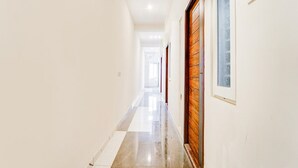 A hallway with a tiled floor, a wooden door, and a light switch on the wall. - Collection O RS Puram North Railway (Coimbatore)