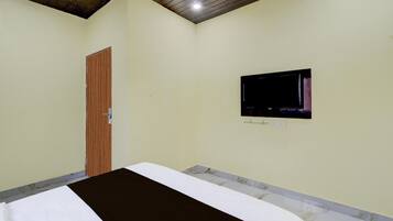 A bedroom with a bed, a wooden door, and a television on the wall.