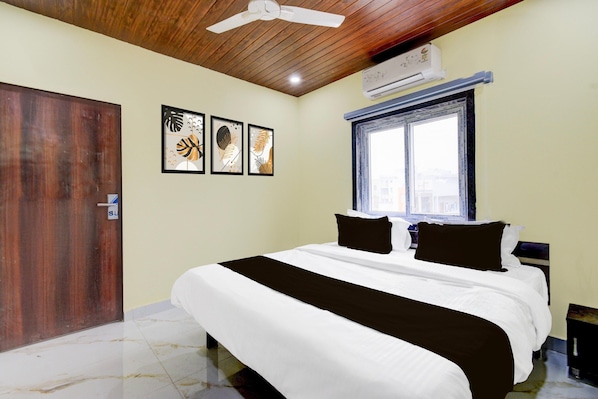 A bedroom with a bed, a ceiling fan, an air conditioning unit, a window, and three framed artworks on the wall. - Super Deluxe Room Hotel Rans (Hyderabad)