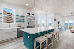Una cocina moderna con una isla grande, armarios blancos y vistas al océano.