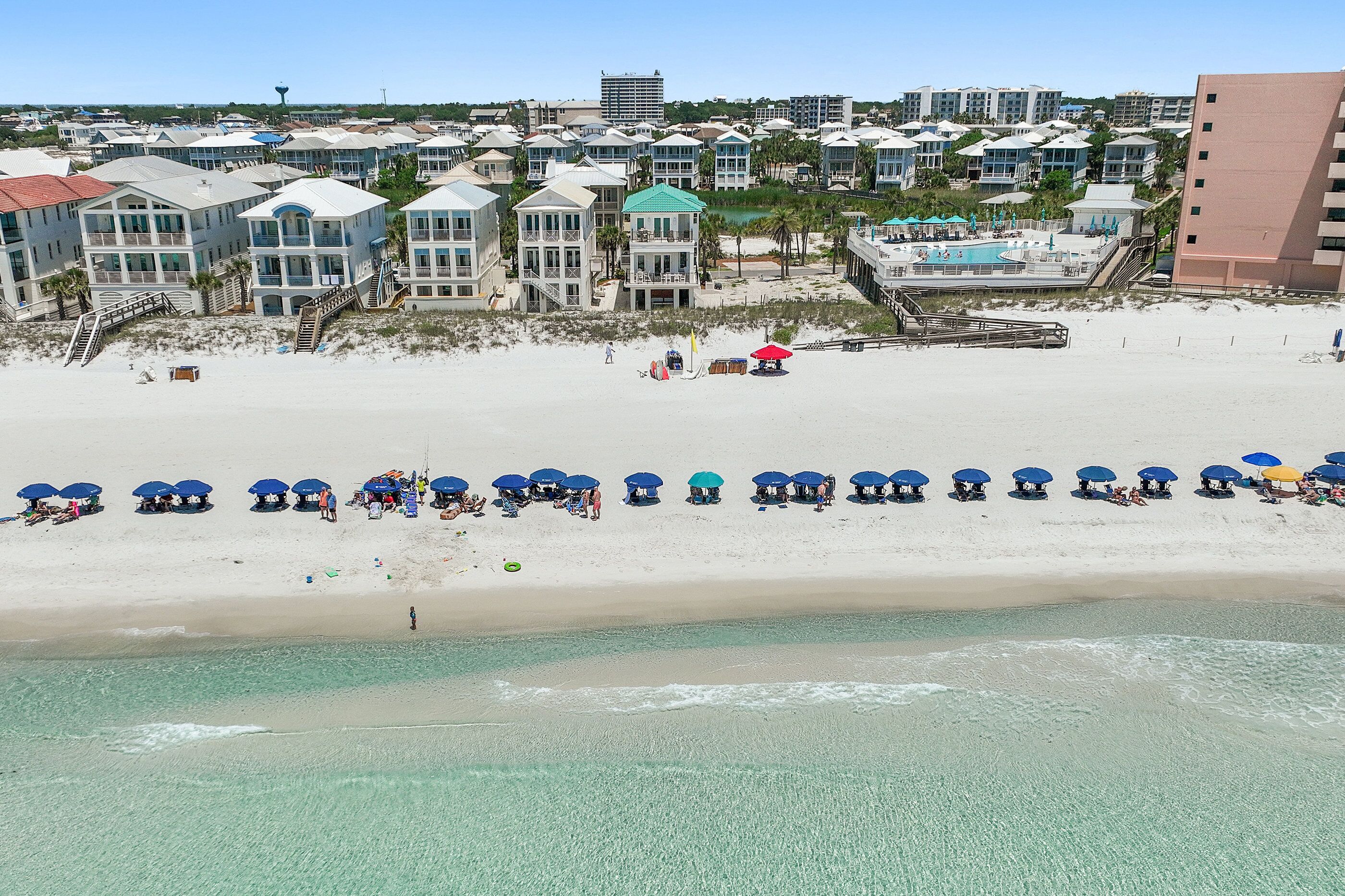 Un hotel frente a la playa con varias construcciones, una playa de arena y una zona de piscina.