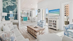 Un salón moderno con un televisor grande, una mesa de centro de madera y vista al mar por la ventana.