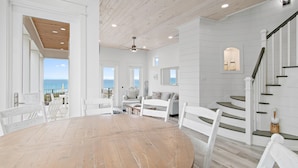 Una habitación amplia con una mesa de comedor de madera, muebles blancos, una escalera y vistas al océano.