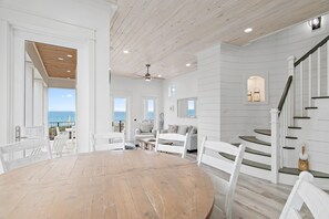Una habitación amplia con una mesa de comedor de madera, muebles blancos, una escalera y vistas al océano.