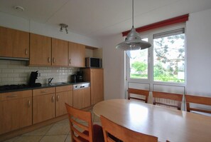A kitchen with wooden cabinets, a microwave, and a dining table with chairs. - Semi-detached Bungalow With Private Sauna (Makkum)