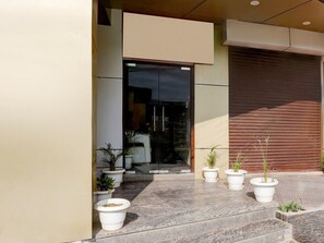 A modern building entrance with a glass door, potted plants, and a closed shutter to the right. - Saver Double OYO Hotel O Sankat Mochan (Varanasi)