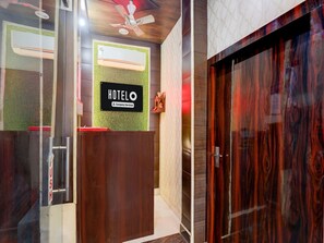 A hotel reception area with a reception desk, a sign reading 'HOTELO Company-Serviced', a ceiling fan, and a wooden door. - Saver Double OYO Hotel O Sankat Mochan (Varanasi)