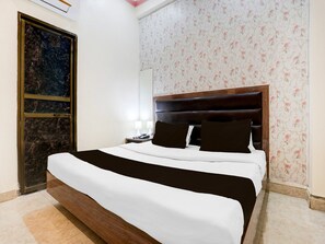 A hotel room with a large bed, a wooden headboard, a nightstand, and a floral wallpaper. - Saver Double OYO Hotel O Sankat Mochan (Varanasi)