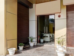 A building entrance with a glass door, potted plants, and a closed shutter door. - Saver Double OYO Hotel O Sankat Mochan (Varanasi)