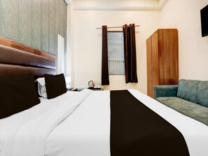 A hotel room with a bed, a sofa, a wardrobe, and a window with curtains. - Saver Double OYO Hotel O Sankat Mochan (Varanasi)
