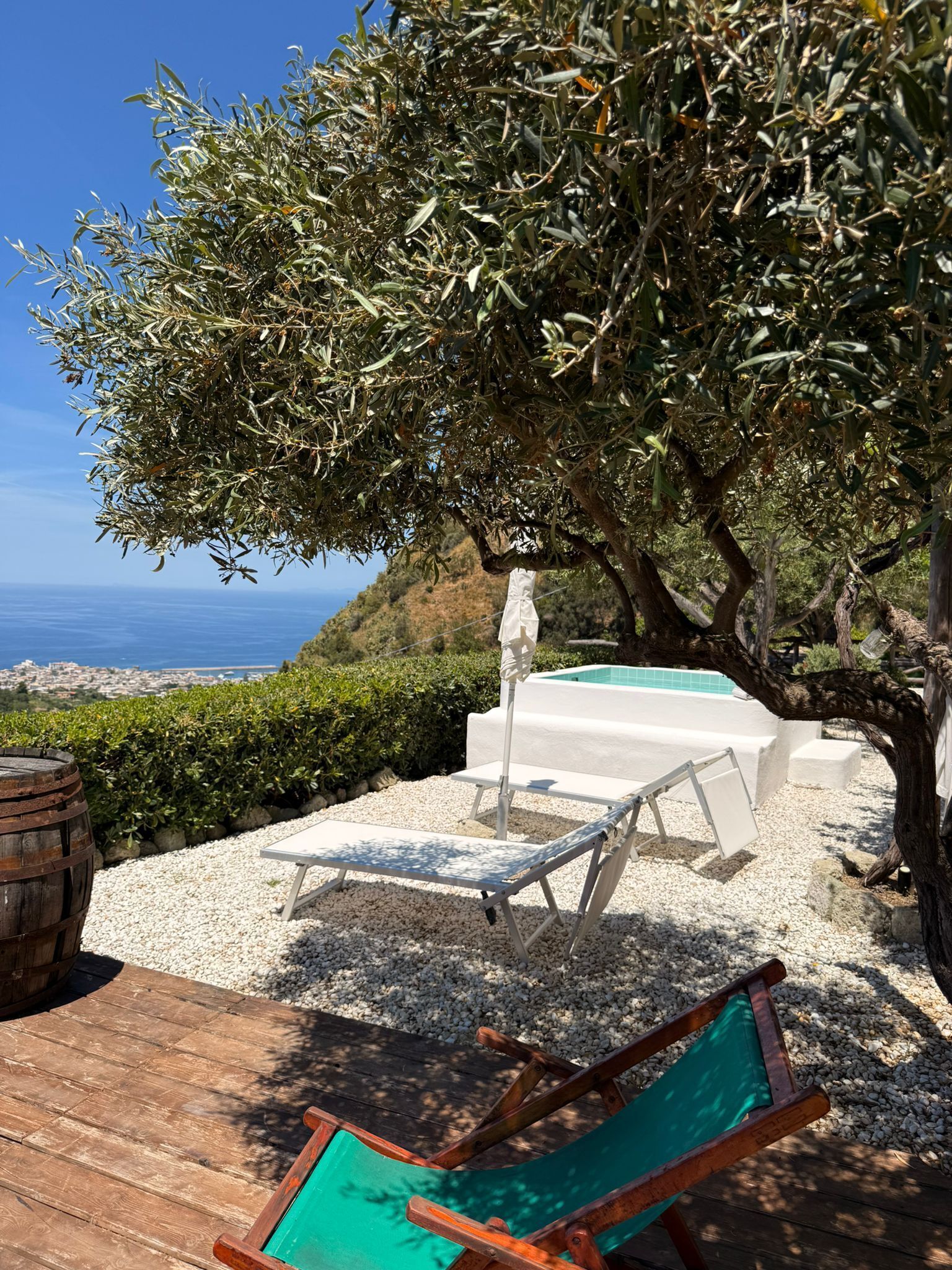 A poolside area with a view of the sea, a wooden deck, and a lounge chair.