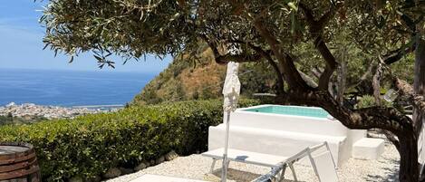 A poolside area with a view of the sea, a wooden deck, and a lounge chair.