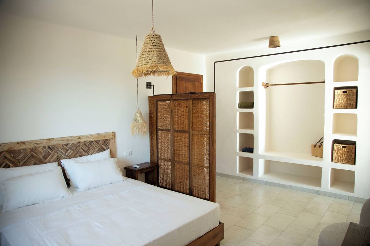A bedroom with a large bed, a wooden headboard, a woven partition, and a white shelving unit with baskets.