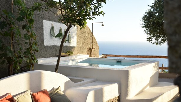 A stone bathtub with a view of the sea, a wooden deck, and a white wall with a plant. - Borgo Corbaro - Exclusive Retreat  (Forio)