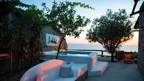 A pool area with a white infinity pool, a white sofa with cushions, and a stone wall with a painting. - Borgo Corbaro - Exclusive Retreat  (Forio)