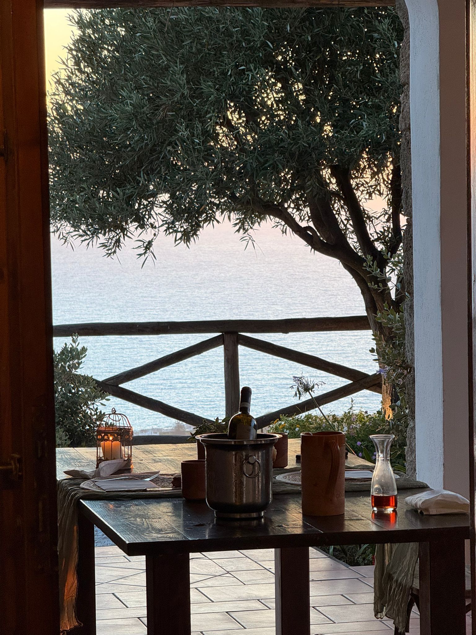 Ein Tisch mit einer Flasche, Kerze und Topfpflanzen mit Blick auf ein Gewässer.