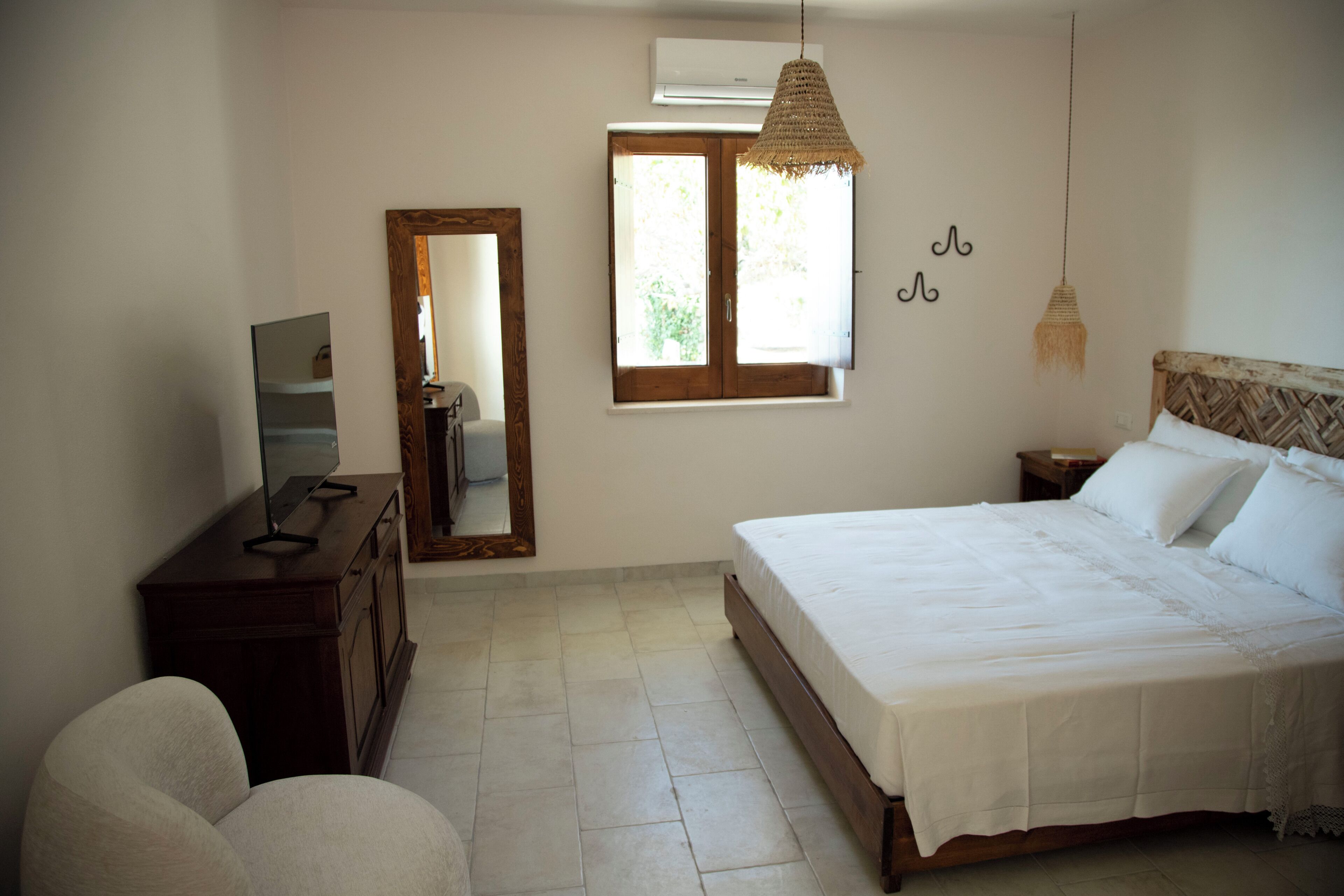 A bedroom with a bed, a dresser, a mirror, a window, and a hanging light fixture.