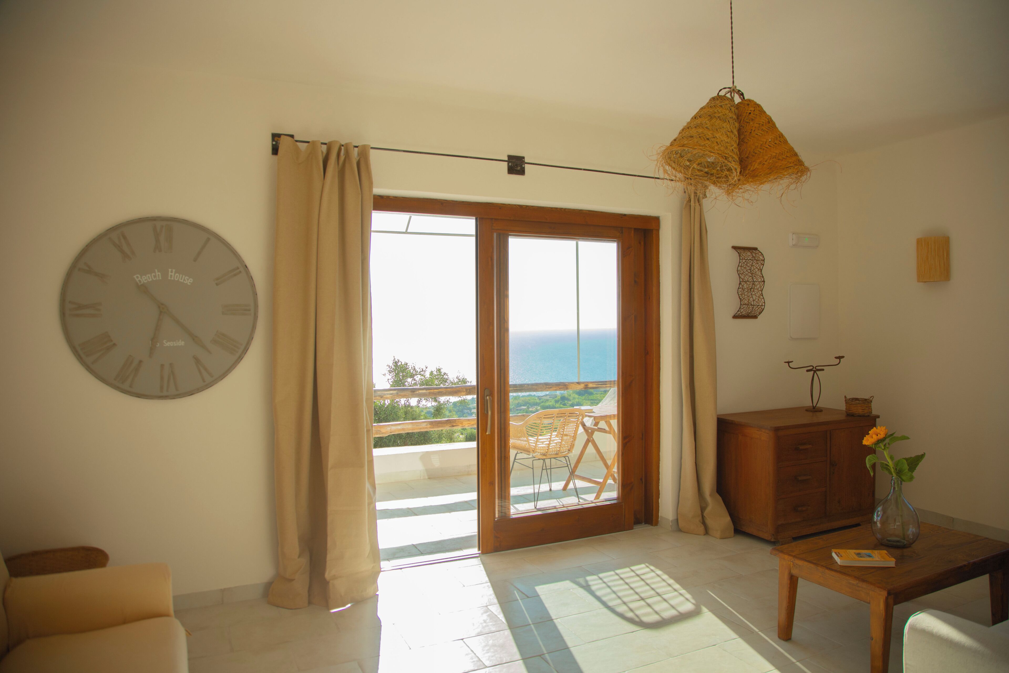 Una habitación con un reloj de pared grande, una mesa de madera con un jarrón, un sofá y vistas al exterior por una puerta corrediza.