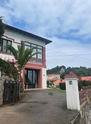 A two-story building with a balcony, a gated entrance, and a pathway leading to the main door. - Perfect getaway in a typical Asturian house with sea views, garden and parking. (Lastres)
