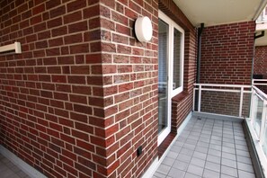 Eine Fassade aus Ziegelsteinen mit einem Fenster und einer Tür, ein gefliester Balkonboden und ein weißes Geländer.