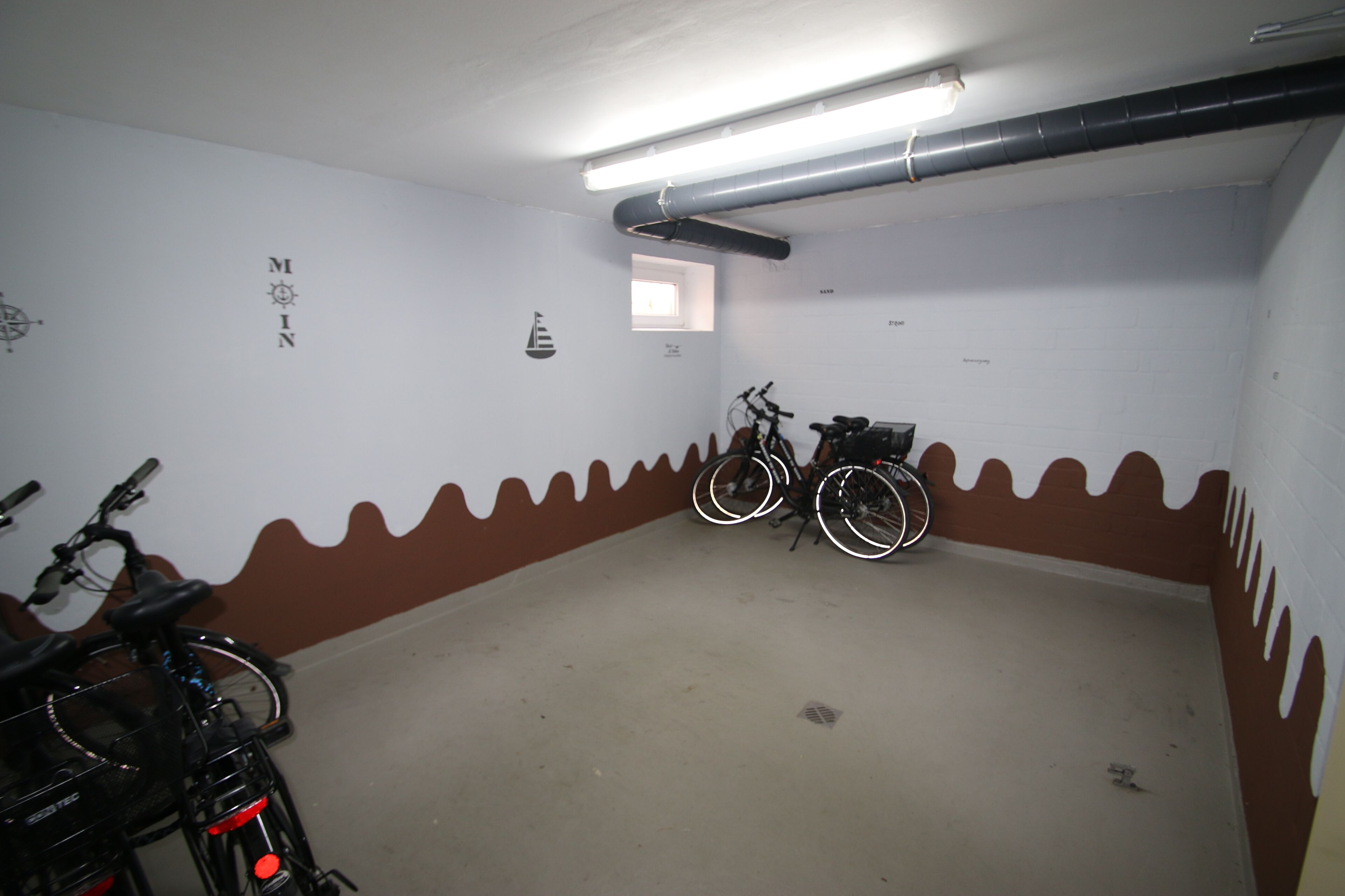 Uma garagem de estacionamento com bicicletas, uma pequena janela e uma parede decorada com motivos náuticos.
