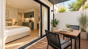 A modern bedroom with a large bed, a kitchenette, and a dining area with a table and chairs. - Escapade à deux · Terrasse privée · Face à Charléty (Paris)