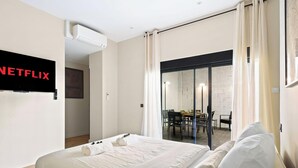 A hotel room with a bed, a TV mounted on the wall, and a sliding glass door leading to a dining area. - Appartement design avec Terasse et climatisation (Paris)