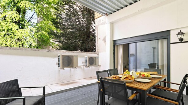 An outdoor dining area with a table set for breakfast, surrounded by chairs, and air conditioning units on the wall. - Appartement design avec Terasse et climatisation (Paris)