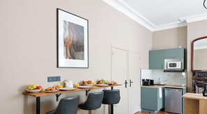 Una cocina moderna con microondas, cafetera y refrigerador pequeño. Hay una mesa de comedor con sillas y un cuadro en la pared.