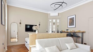 A modern living room with a sofa, a flat-screen TV, a dining area with a table and chairs, and a hallway with a mirror. - Prestige appartement à Paris (Paris)