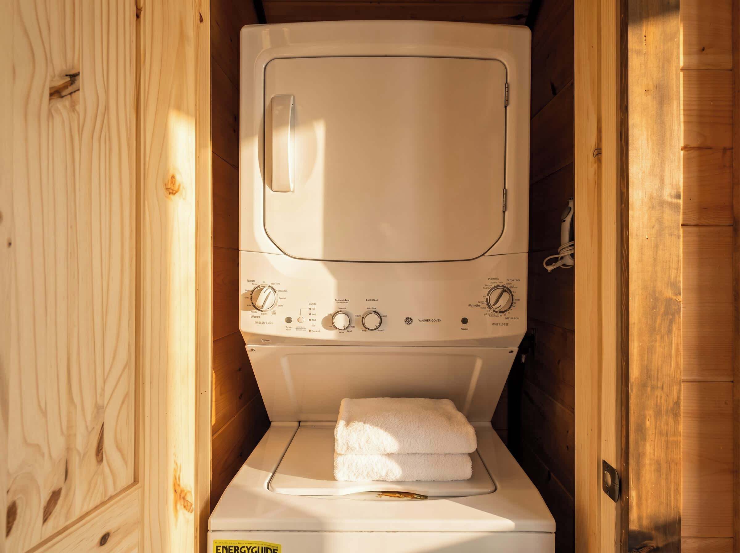A compact, wooden-walled laundry room with a white washing machine and a folded towel on the dryer.