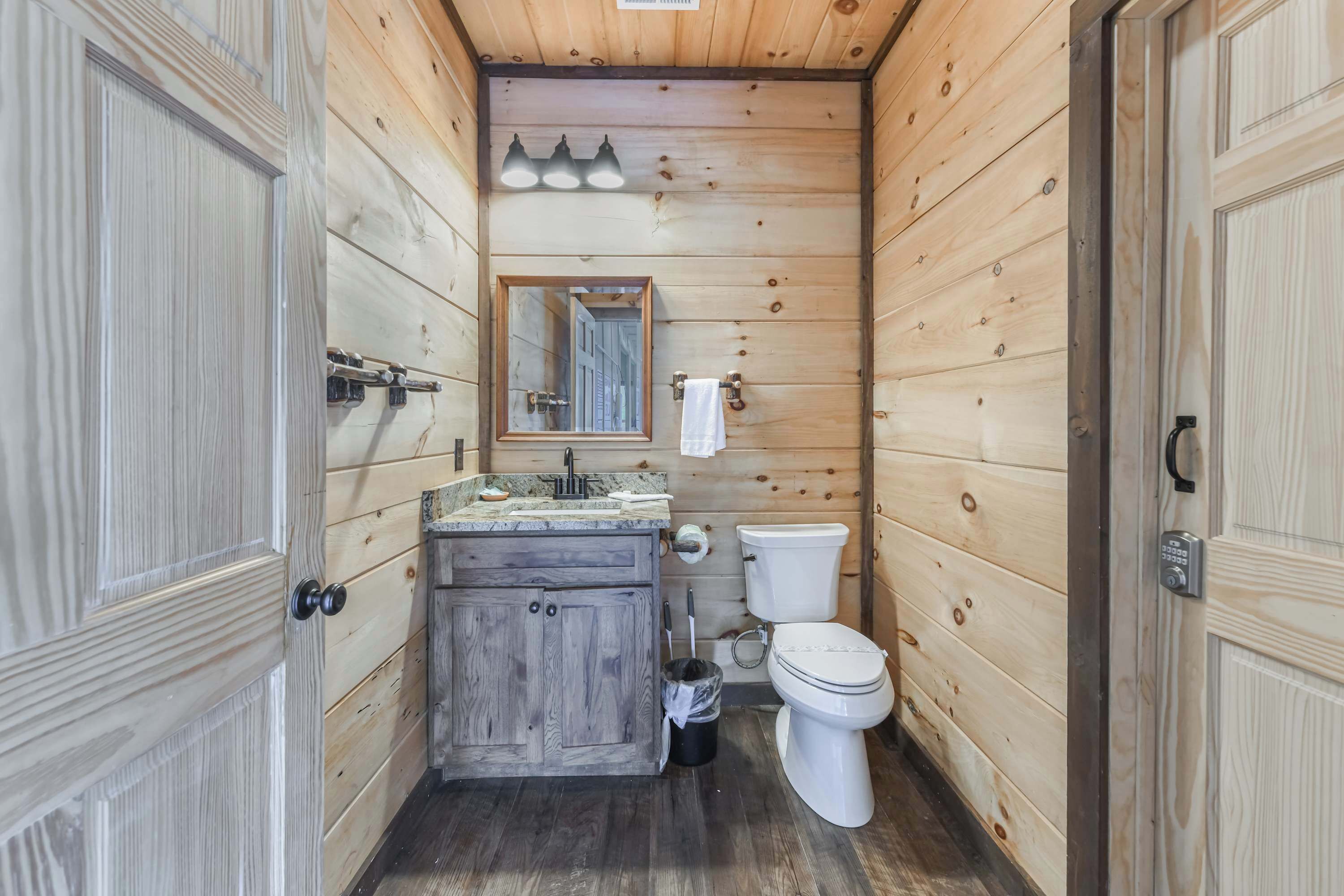 A compact wooden bathroom with a sink, mirror, toilet, and cabinets.