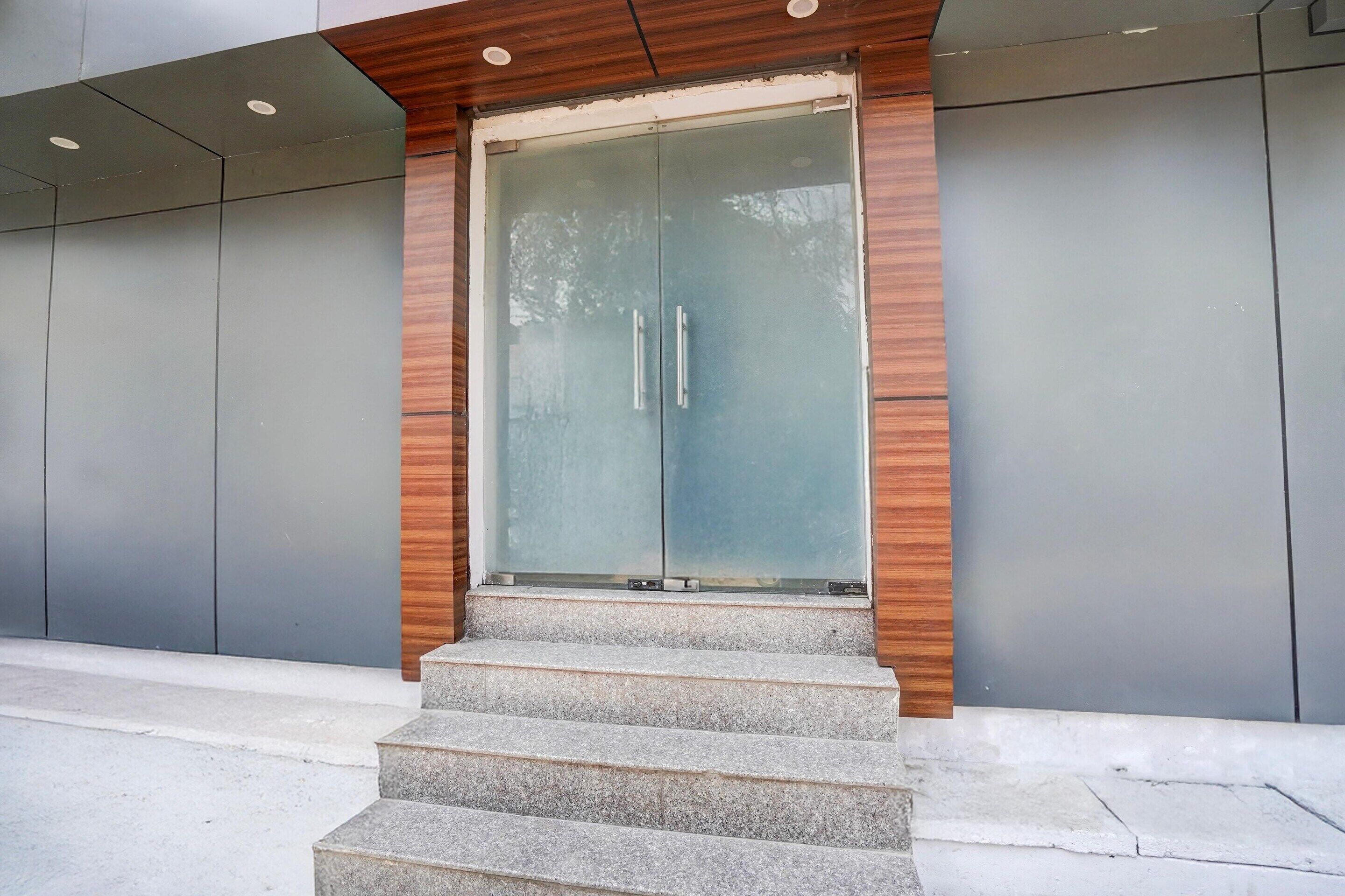 A modern building entrance with a glass door, wooden trim, and a set of concrete steps leading up to it.