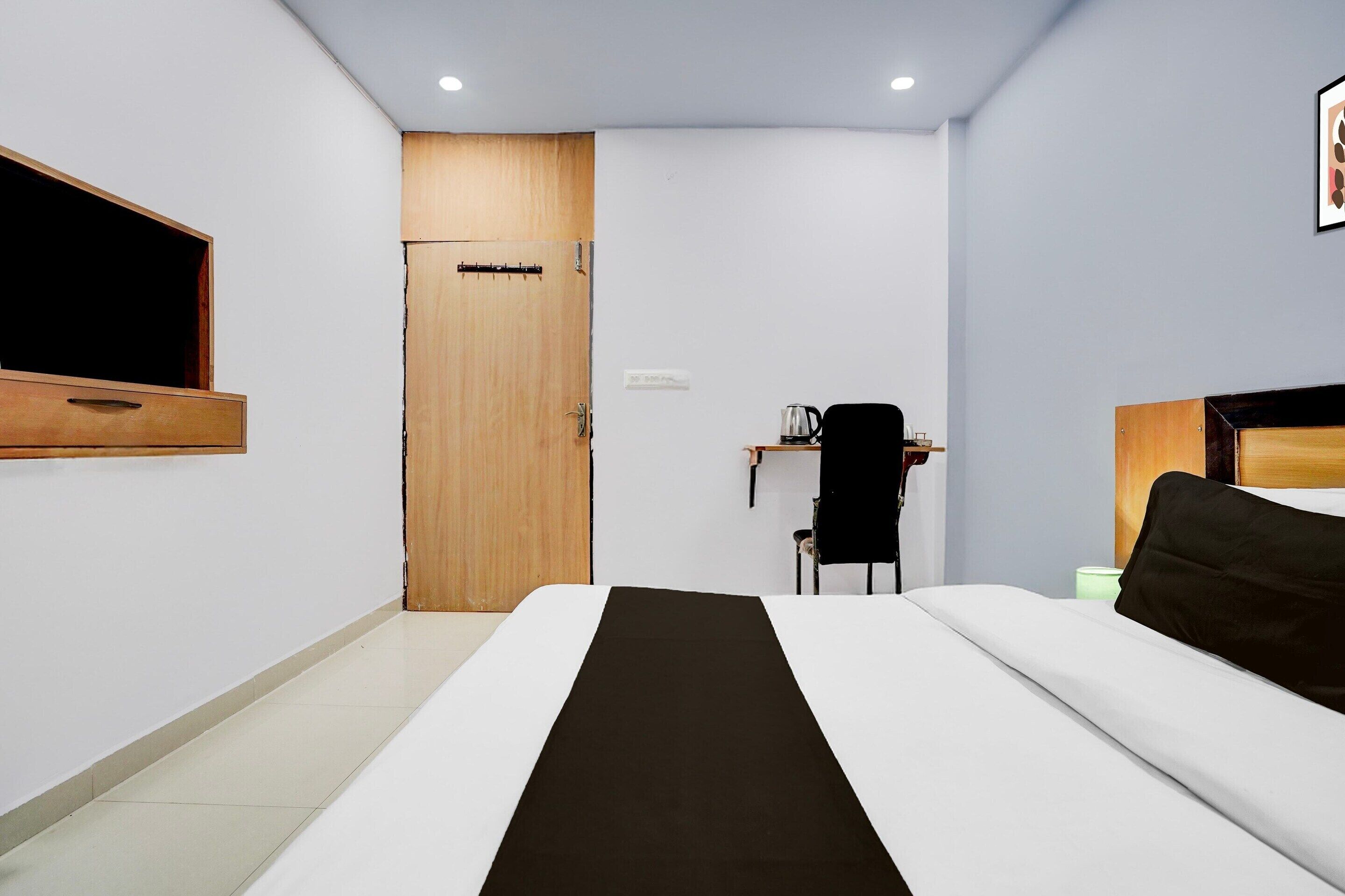 A hotel room with a bed, a wooden door, a desk with a chair, and a wall-mounted TV.