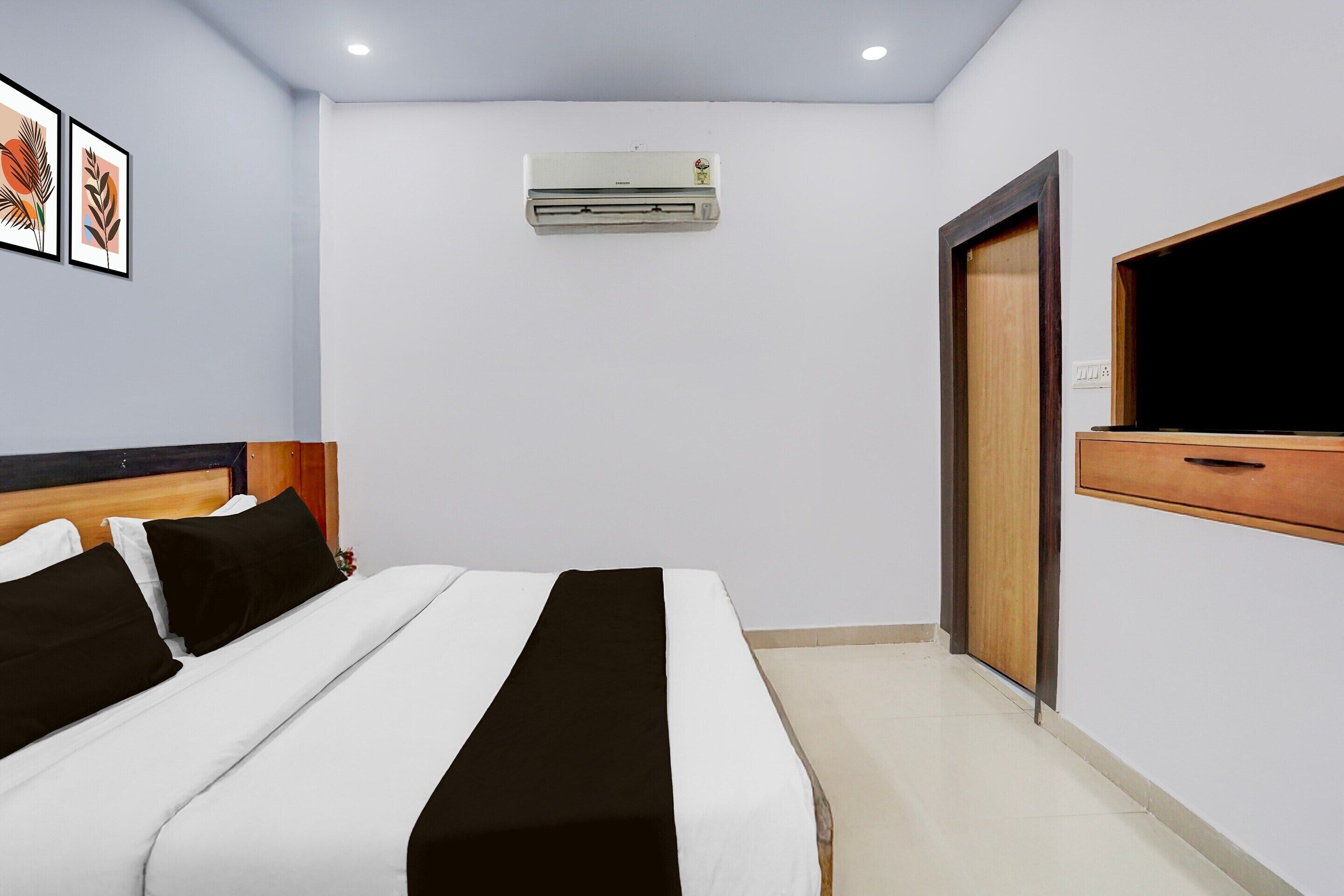 A hotel room with a bed, an air conditioner, a TV, and a wooden door.