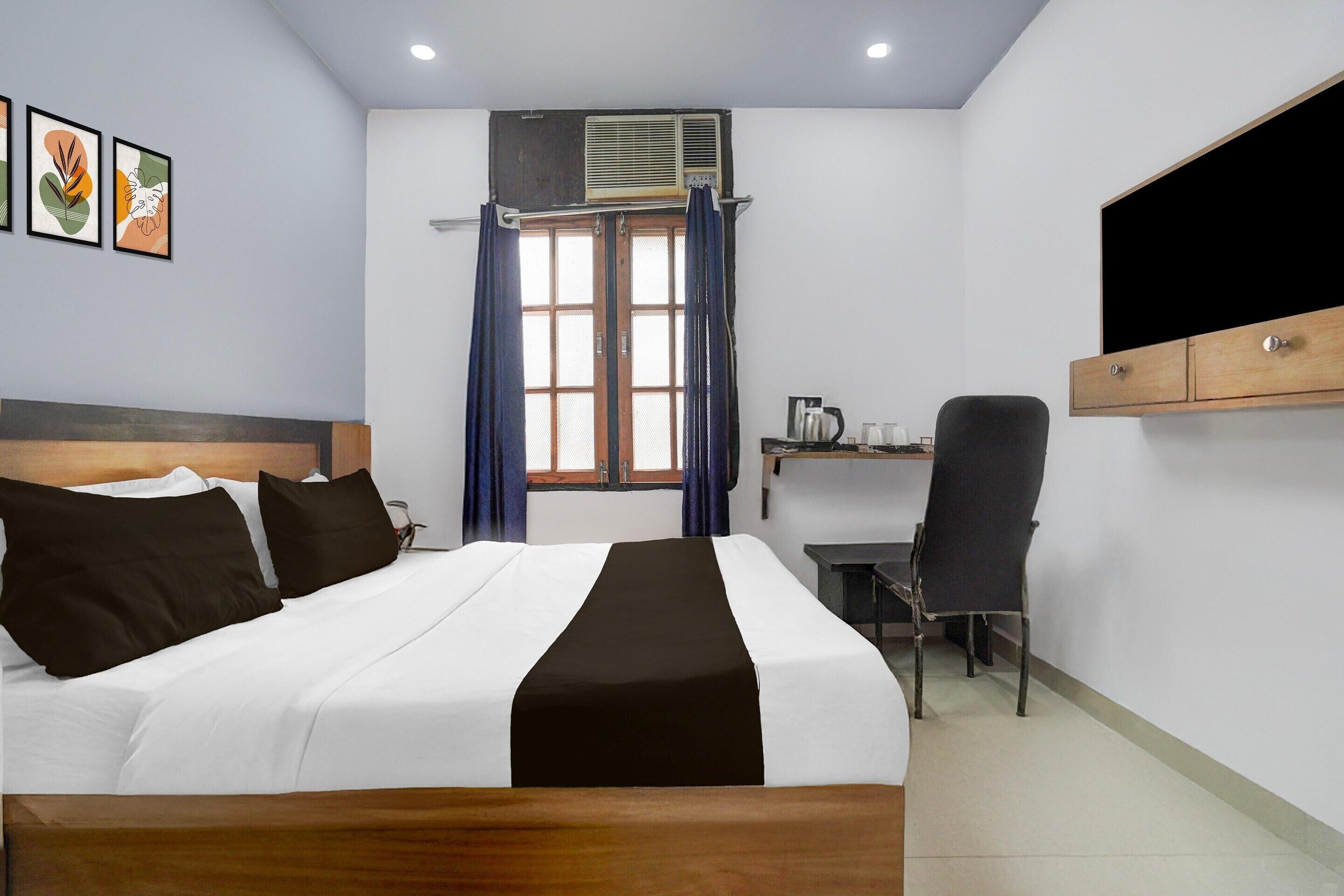 Une chambre d’hôtel avec un lit, un bureau, une chaise, une télévision et une fenêtre avec des rideaux.