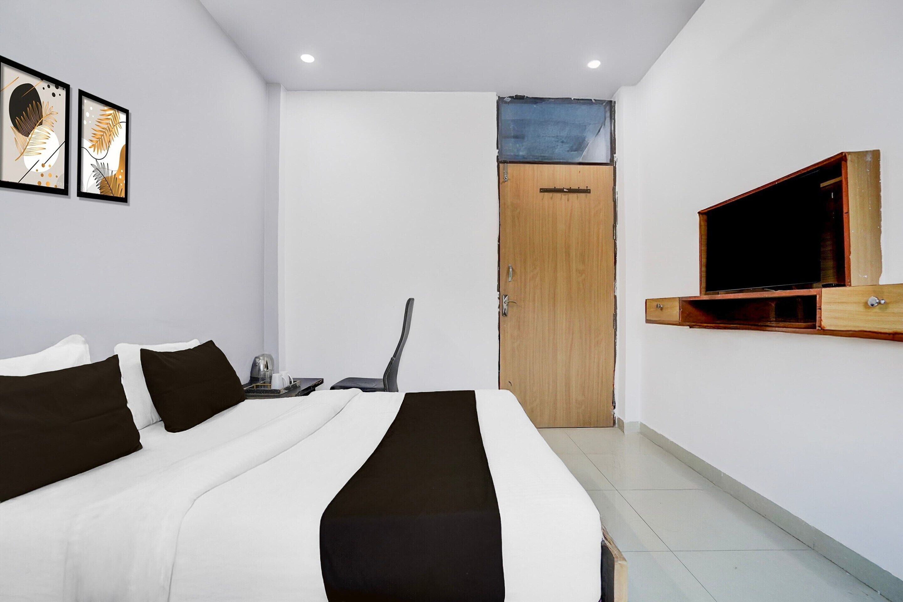 A hotel room with a bed, a desk, a chair, a television, and a door.