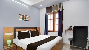 Une chambre d’hôtel comprenant un lit, une table de chevet, une lampe, un appareil de climatisation, une fenêtre avec des rideaux et une chaise.