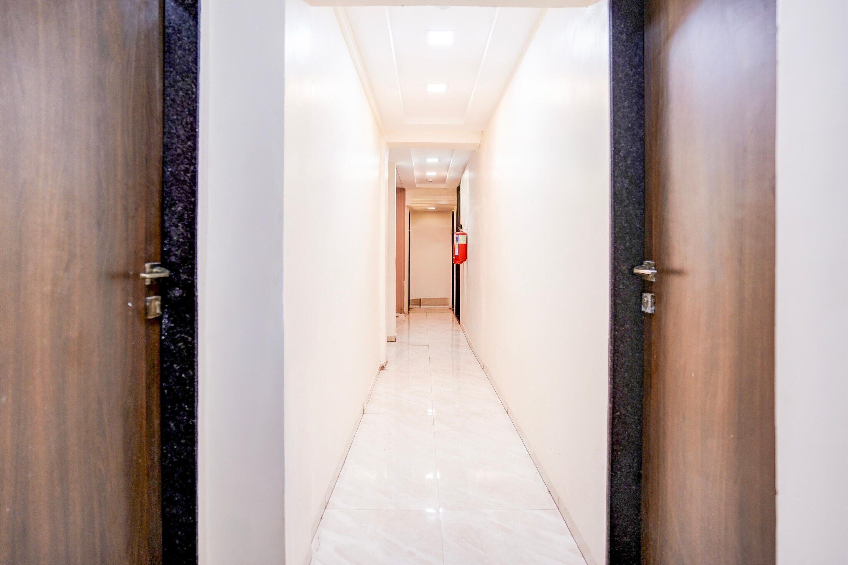 A corridor with two wooden doors, a fire extinguisher, and a tiled floor.