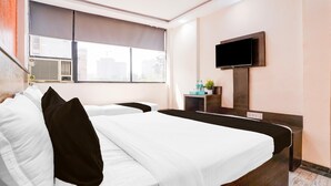 Habitación de hotel con dos camas, un televisor montado en la pared, un equipo de aire acondicionado y una ventana con vistas a edificios.