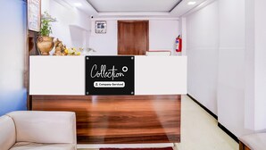 Un mostrador de recepción con un cartel que dice 'Collection', una puerta de madera, un extintor y una planta.