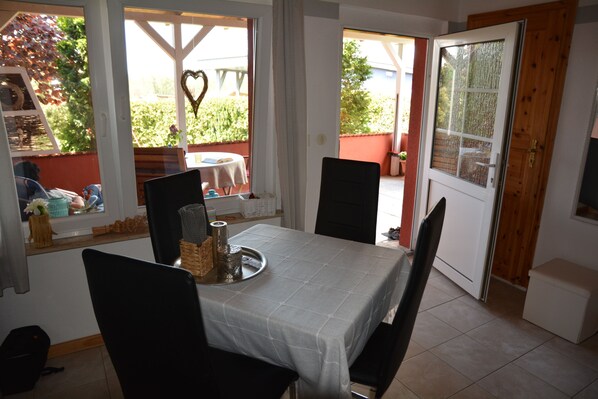 A dining area with a table set for two, chairs, a window with a heart decoration, and a view of a garden.