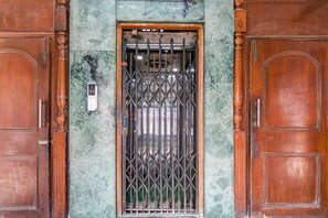 Una puerta de madera con una reja de seguridad metálica, un muro de mármol y un pequeño dispositivo electrónico en la pared.