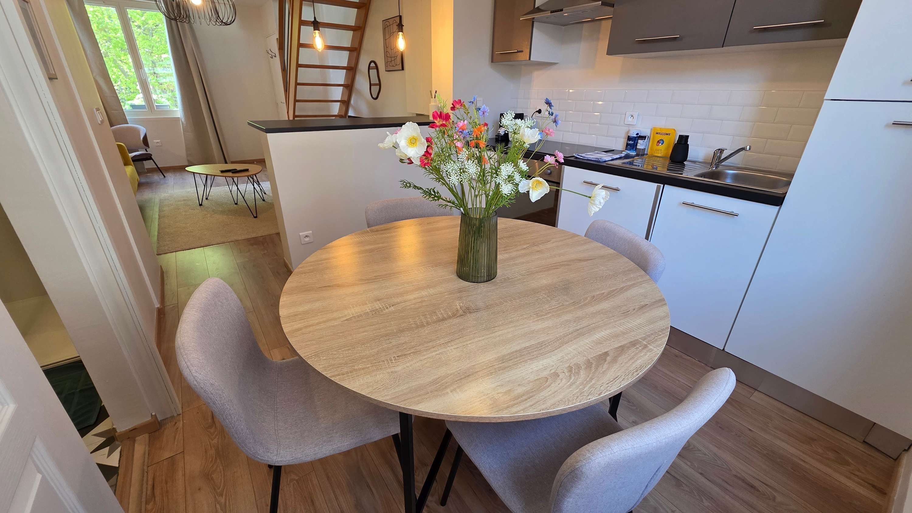 Une cuisine moderne avec une table ronde en bois, des chaises à revêtement gris et un vase rempli de fleurs.
