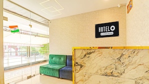 Uma área de recepção de hotel com um balcão de mármore, um sofá verde e azul, e uma placa indicando que o hotel oferece serviços corporativos.