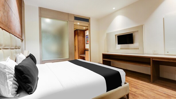 A hotel room with a bed, a TV, a desk, and a wardrobe. - Saver Doublekey Rooms (New Delhi)