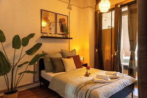 Una cama bien hecha con almohadas, una mesita de noche con lámpara y una planta en maceta.